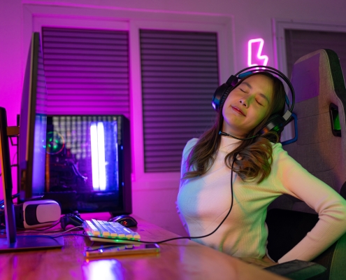 Young people Backache. Gamer and E-Sport online of Asian woman playing online computer video game with lighting effect, broadcast streaming live at home. She a backache due to sitting for a long time