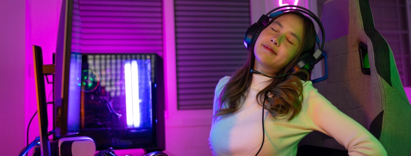 Young people Backache. Gamer and E-Sport online of Asian woman playing online computer video game with lighting effect, broadcast streaming live at home. She a backache due to sitting for a long time